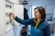 Žena nastavuje páčku hlavního jističe v otevřeném rozvaděči v chodbě bytu.
