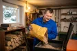 Muž sype pelety z pytle do zásobníku peletového kotle v kotelně vedle dřeva a briket.